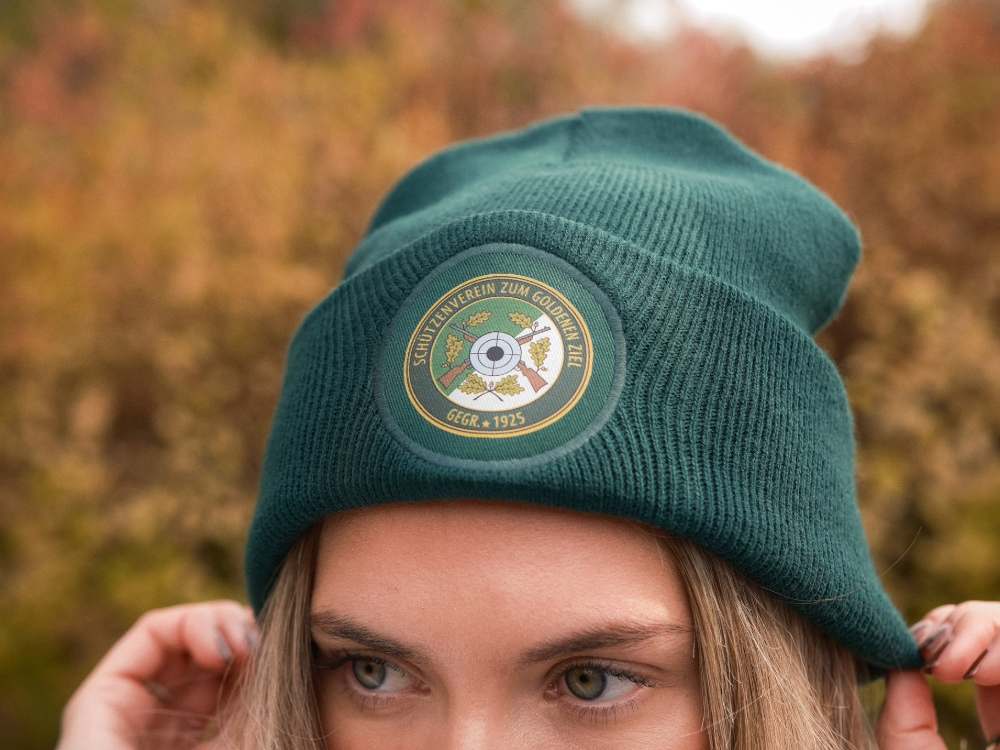 Grüne, personalisierte Strickmütze (Beanie) von Mister Merch mit einem gestickten oder gedruckten Logo des Schützenvereins "Zum Goldenen Ziel", gegründet 1925.